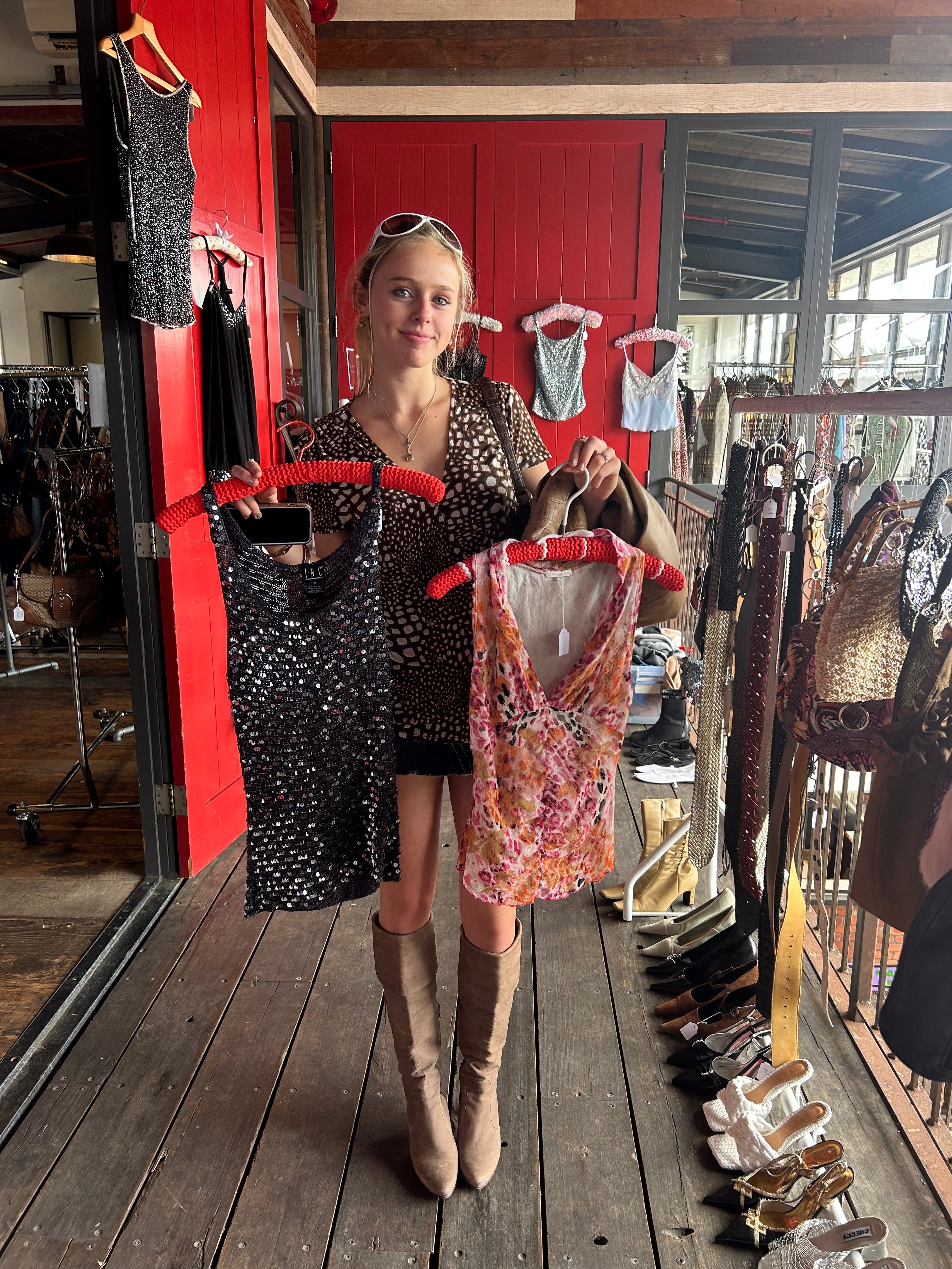 Person holding a patterned dress in a store setting with clothing racks and a red cabinet.