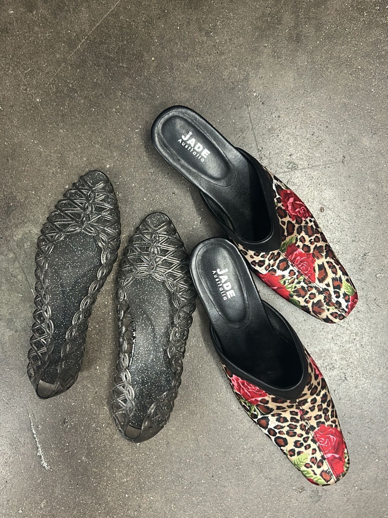 Pair of black flat shoes with braided sole and leopard print slip-on shoes on a concrete floor.